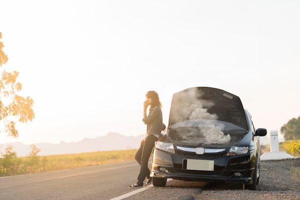 A woman is standing next to a broken down car on the side of the road. | Lex Brodies 