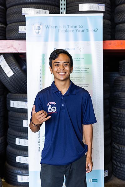 A man in a blue shirt is standing in front of a stack of tires. | Lex Brodies
