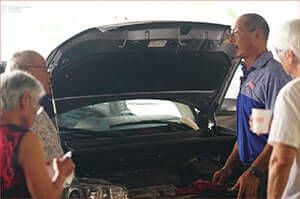A group of people are looking under the hood of a car. | Lex Brodies 