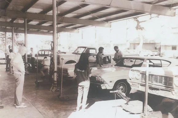 A black and white photo of people working on cars in a garage | Lex Brodies