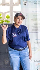 A woman in a blue shirt and jeans is standing in front of a sign. | Lex Brodies 