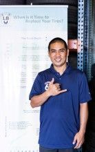 A man in a blue shirt is standing in front of a sign giving a thumbs up. | Lex Brodies