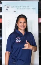 A woman in a blue shirt is standing in front of a sign that says `` when is it time to replace your tires ? '' | Lex Brodies