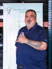 A man with a tattoo on his arm is standing in front of a sign. | Lex Brodies