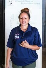 A woman wearing a blue polo shirt is standing in front of a sign. | Lex Brodies 