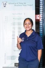 A woman in a blue shirt is standing in front of a sign that says `` when is it time to replace your tires ? '' | Lex Brodies 