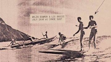 A group of people are standing on a beach holding surfboards. | Lex Brodies