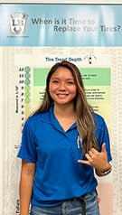 A woman in a blue shirt is standing in front of a sign that says `` when is it time to replace your tires ''. | Lex Brodies 