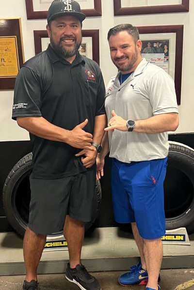 Two men are standing next to each other in front of a tire. | Lex Brodies