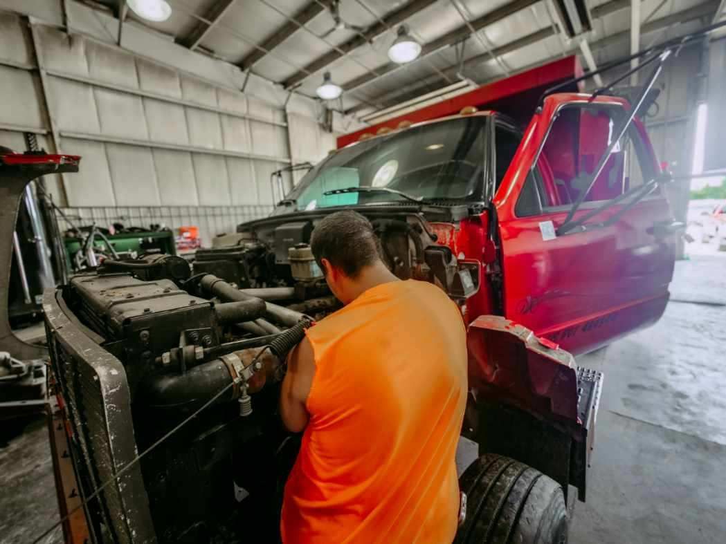 A man in an orange shirt is working on a red truck in a garage.