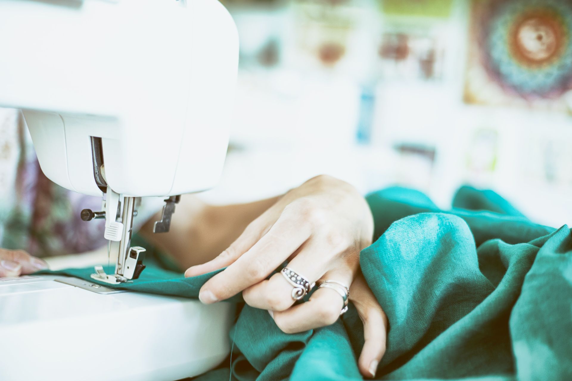A woman is using a sewing machine to sew a piece of green fabric.