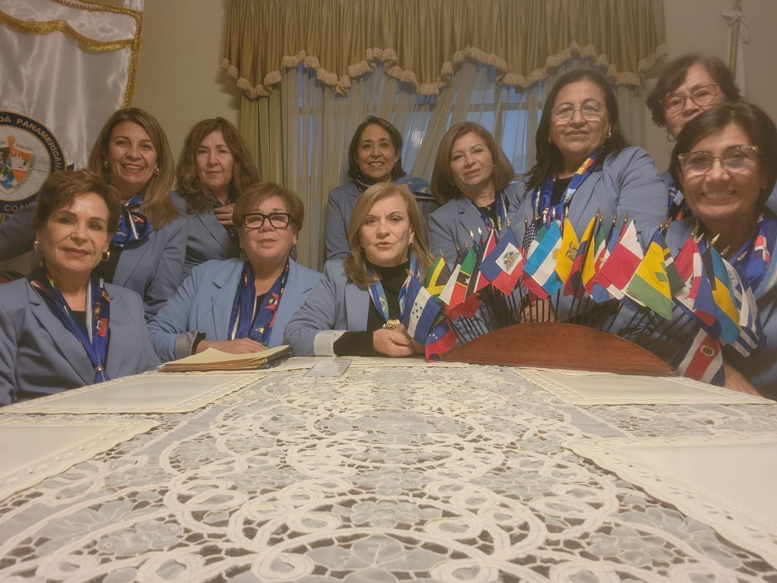 Group of women in light blue jackets, flags on table.