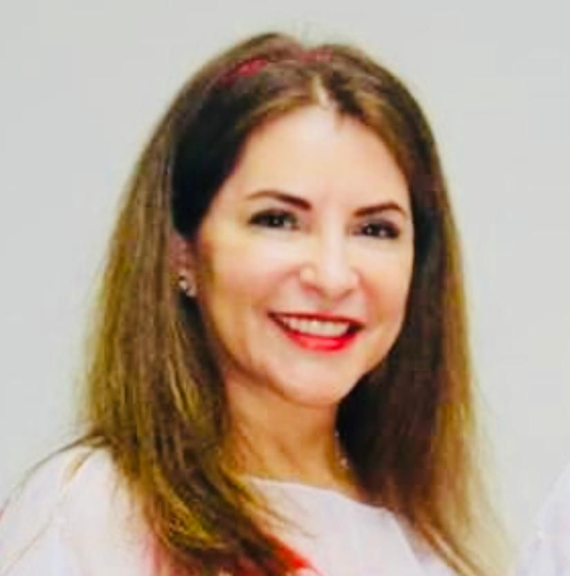 Woman with long brown hair smiles, wearing a white top with red accents.