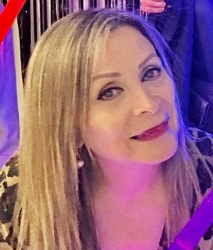 Woman with blonde hair smiles, wearing pearl earrings and a leopard-print top.