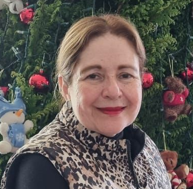 Woman wearing a leopard-print vest smiling in front of a Christmas tree with red ornaments and a snowman decoration.