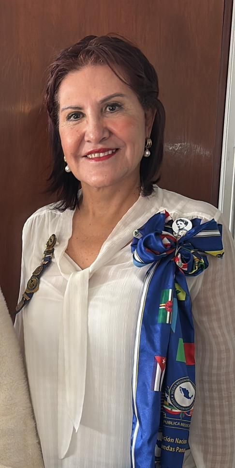 Woman with dark hair smiles, wearing a white blouse and a blue scarf with logos.