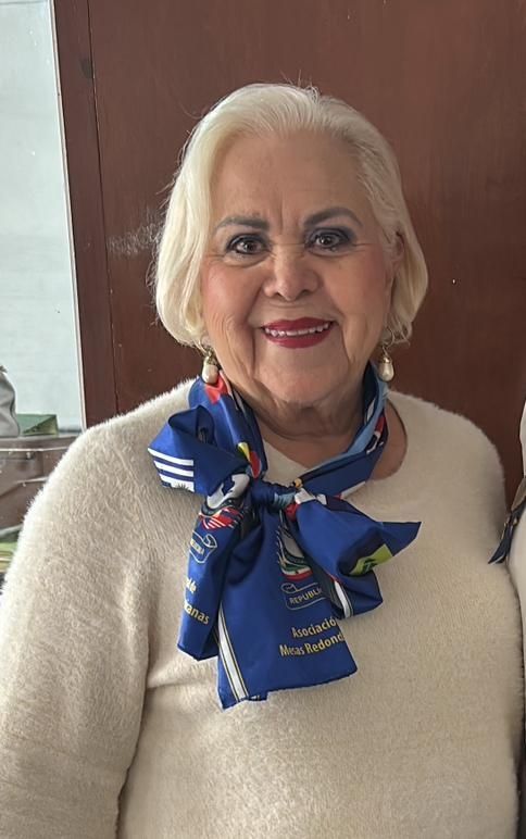 Woman with blonde hair wearing a cream sweater and blue scarf. She is smiling.