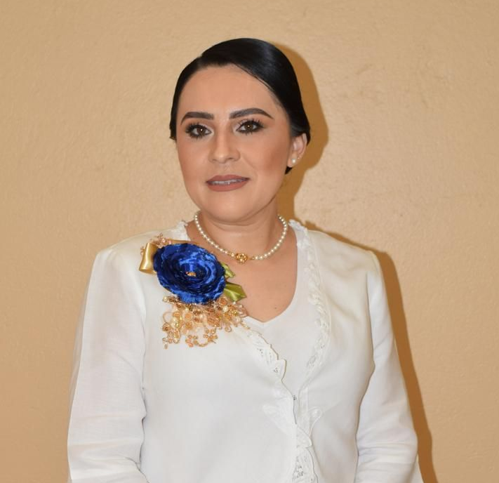 Woman in white blouse with blue floral brooch and pearl necklace.