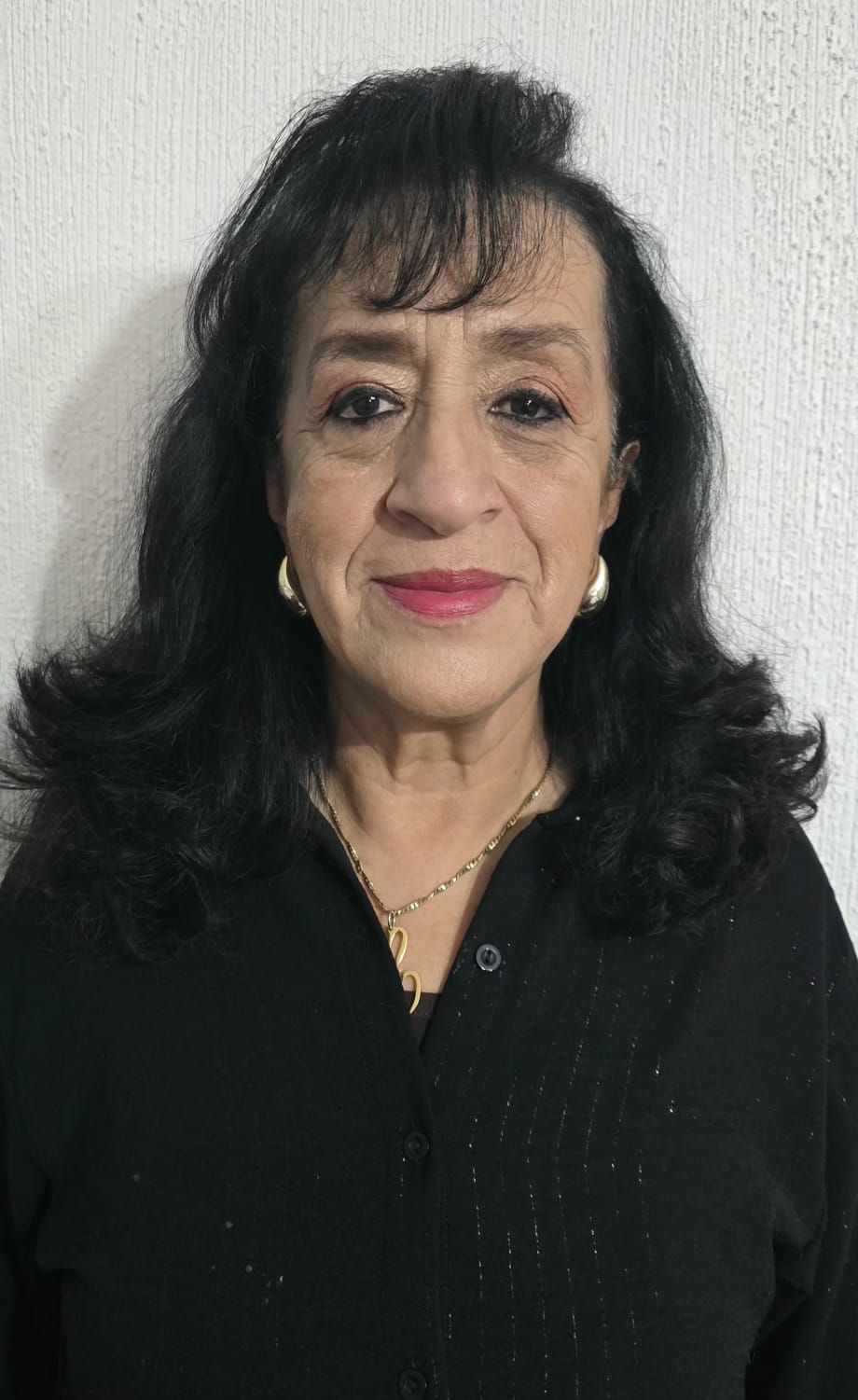 Woman with dark hair, wearing a black shirt and gold jewelry, smiles at the camera.