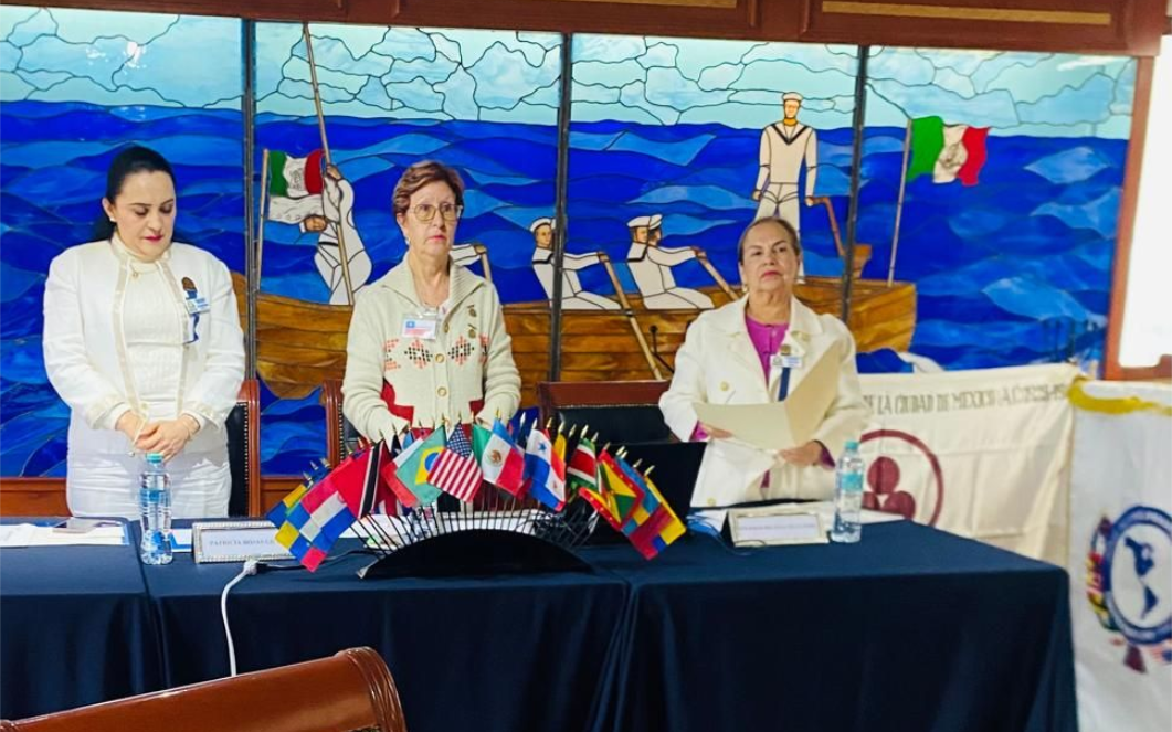 Three women at a table with international flags. Background has a nautical mural.