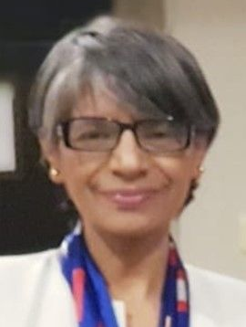 Woman with short gray hair and glasses smiles, wearing a white jacket and a scarf with red and blue details.