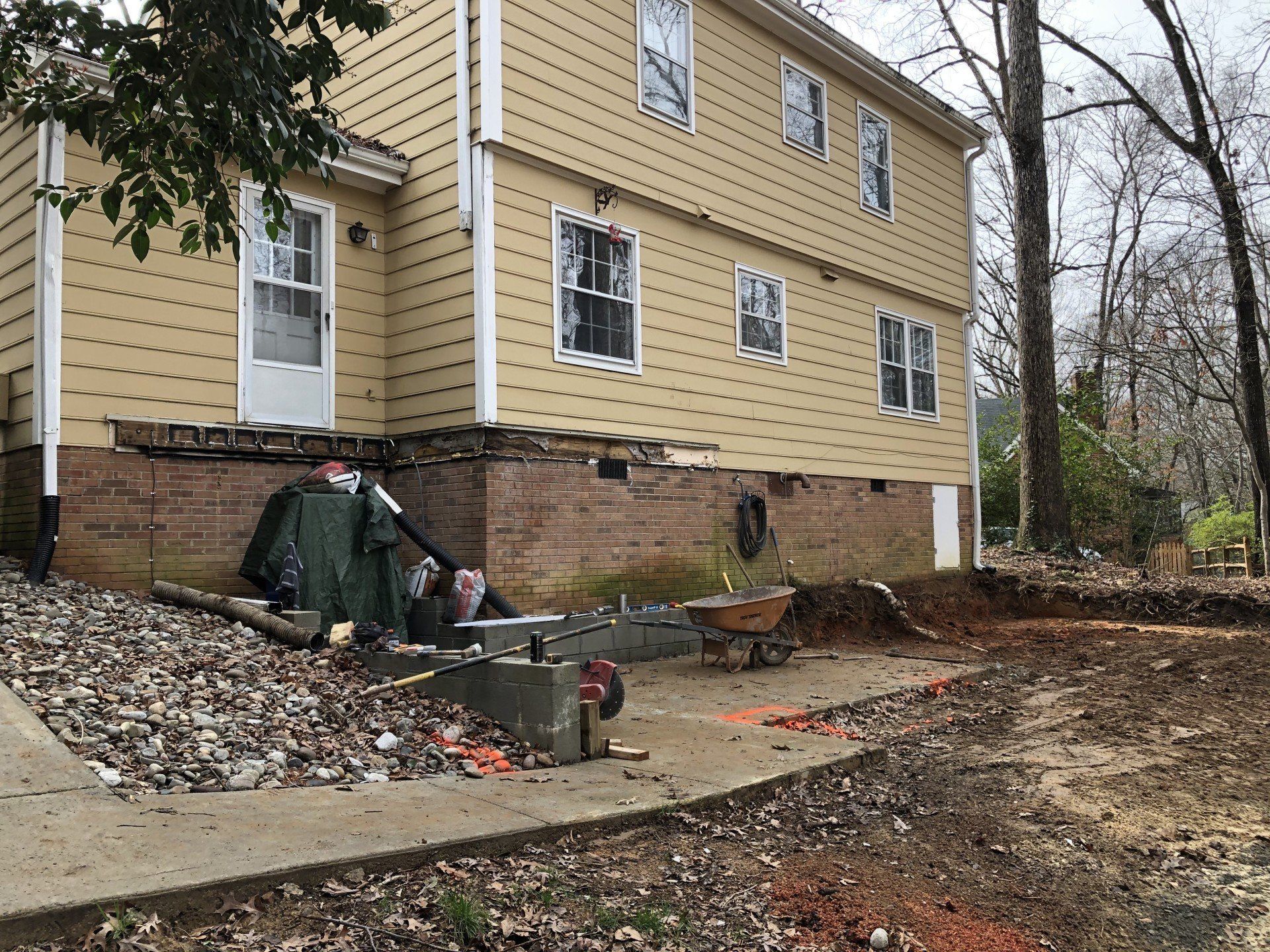 A large yellow house is being remodeled with a wheelbarrow in front of it.