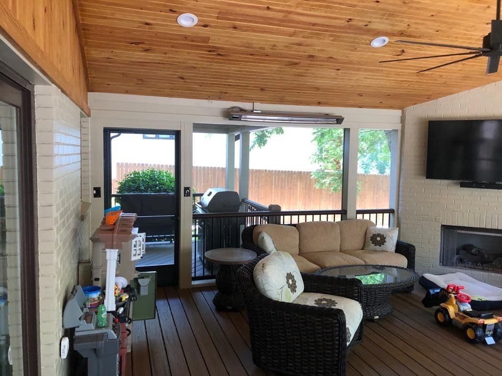 A screened in porch with a couch , chairs , table and television.