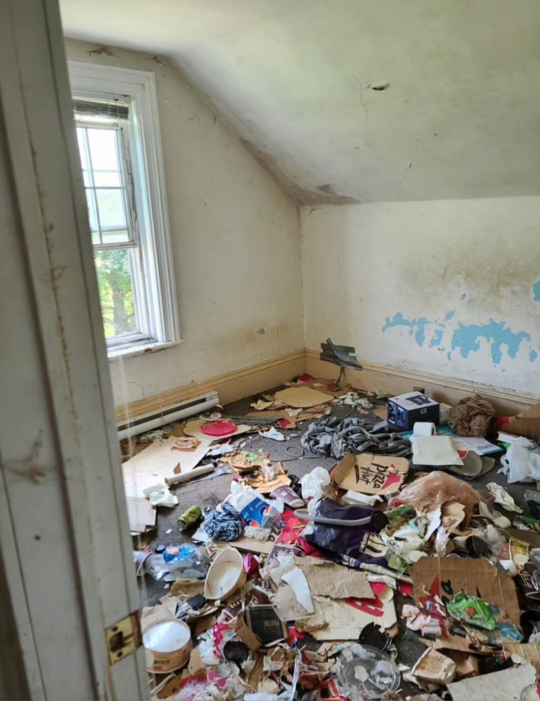 A room with a lot of trash on the floor and a window.