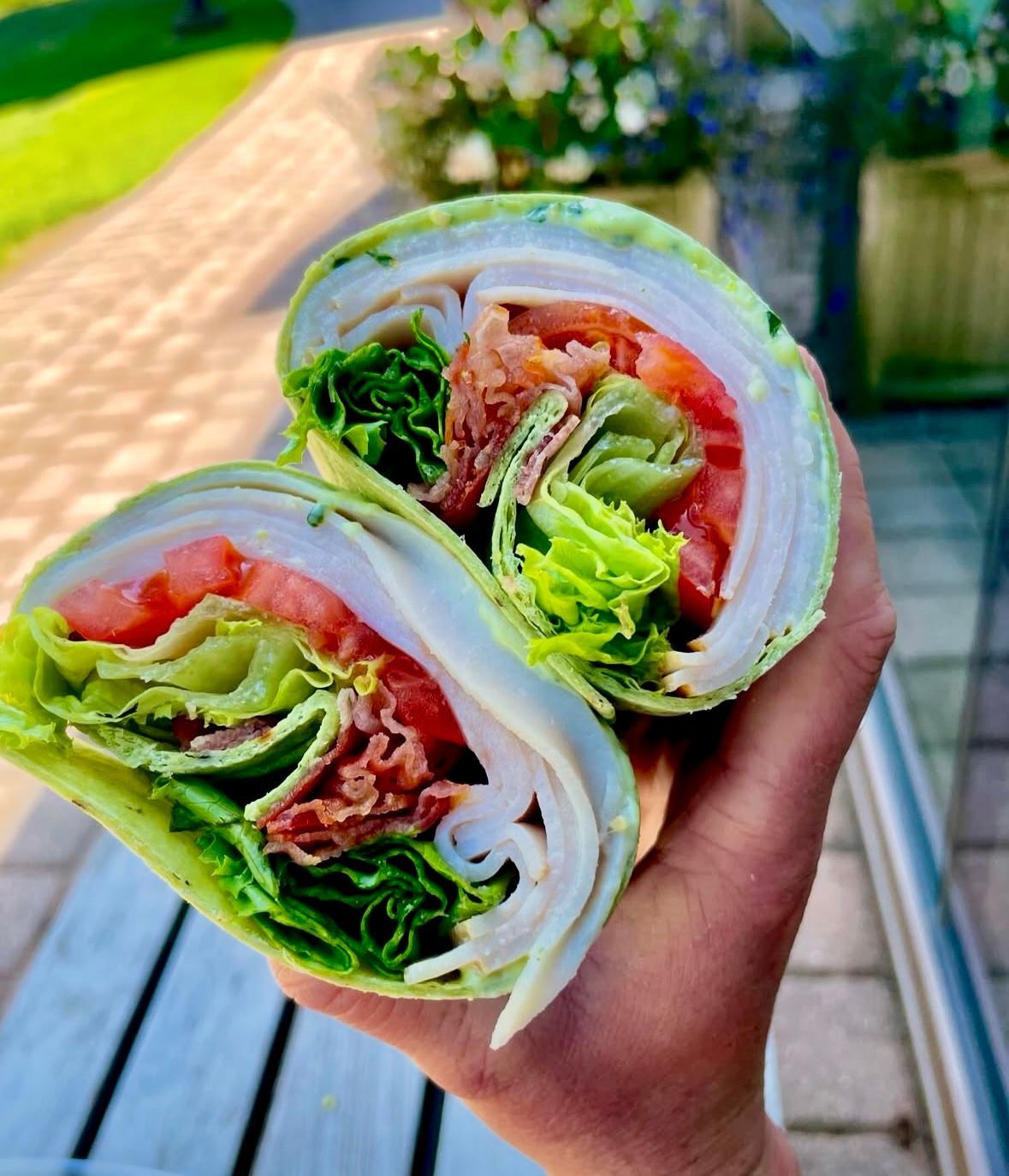 Hand holding a cut wrap filled with turkey, lettuce, tomato, and bacon.