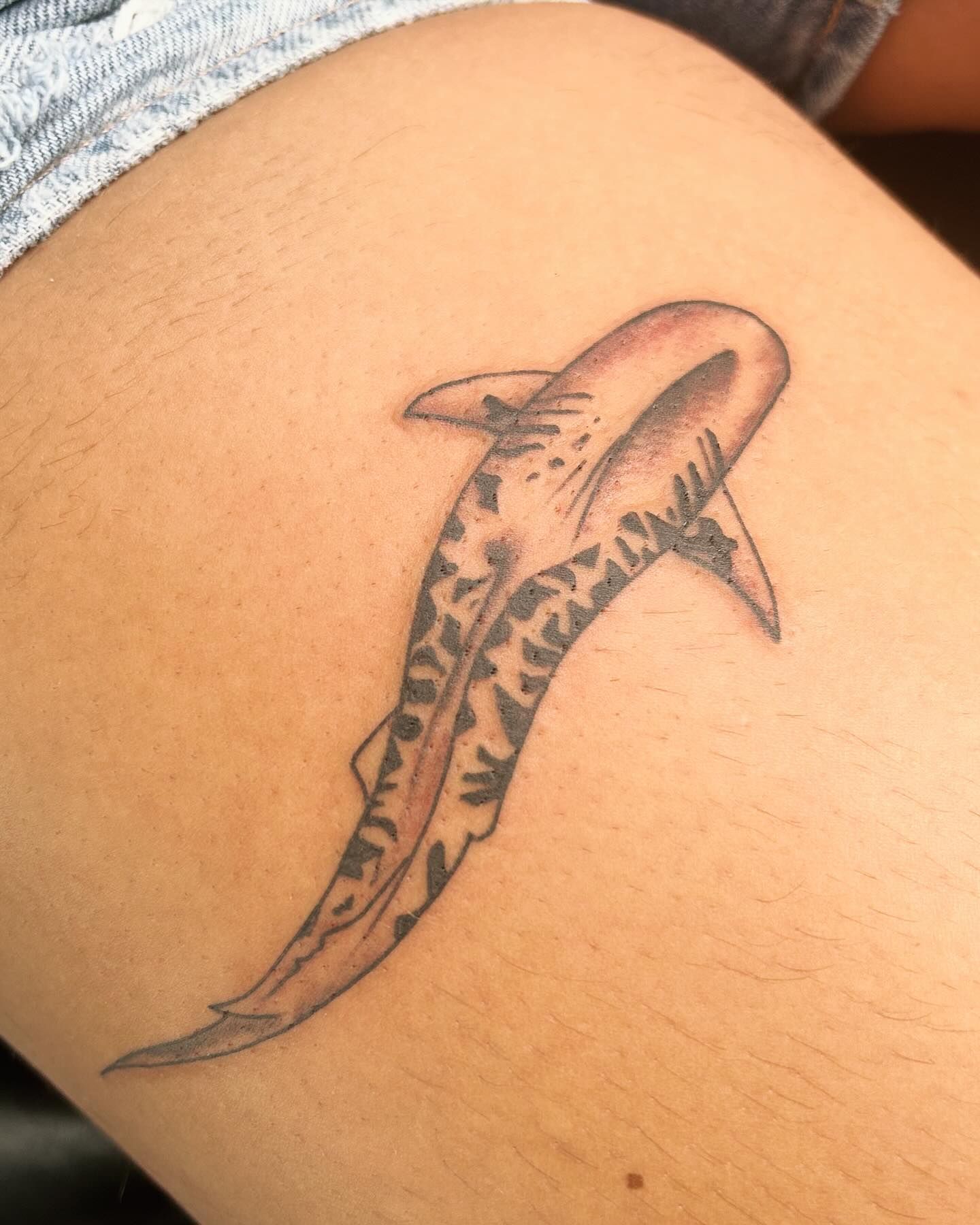 A woman has a tattoo of a shark on her leg