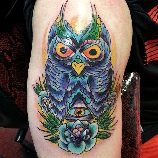 A colorful tattoo of an owl with flowers and an eye