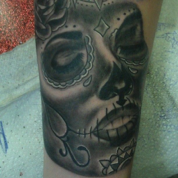 A black and white tattoo of a sugar skull on a person 's arm
