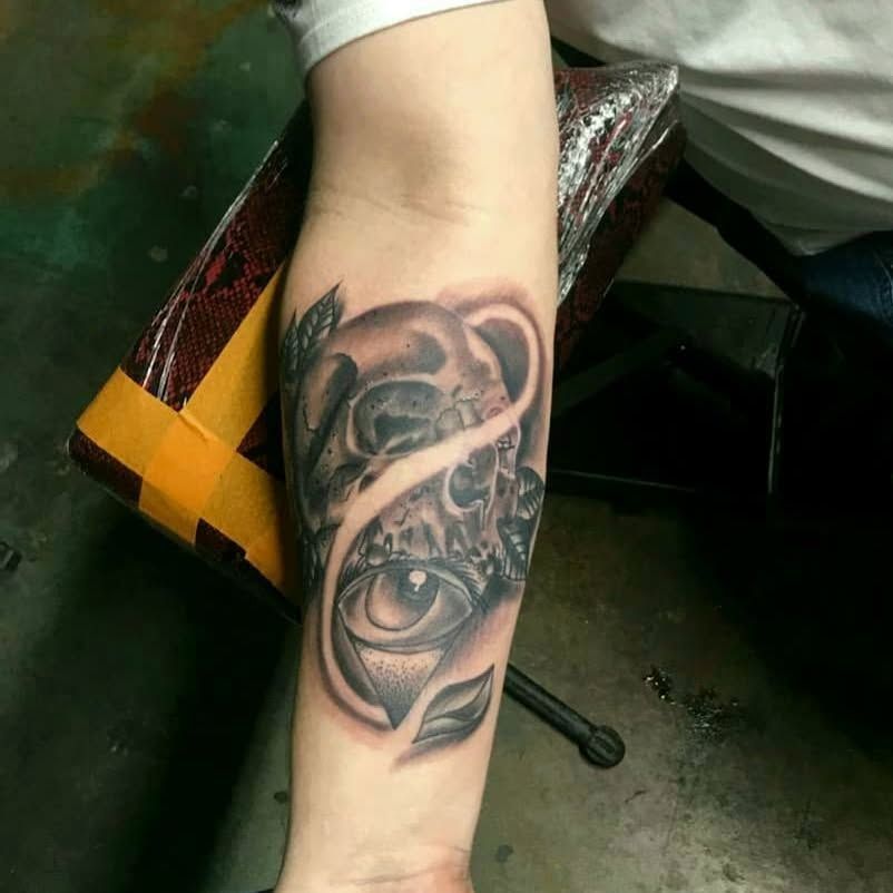 A person has a tattoo of a skull and an eye on their forearm