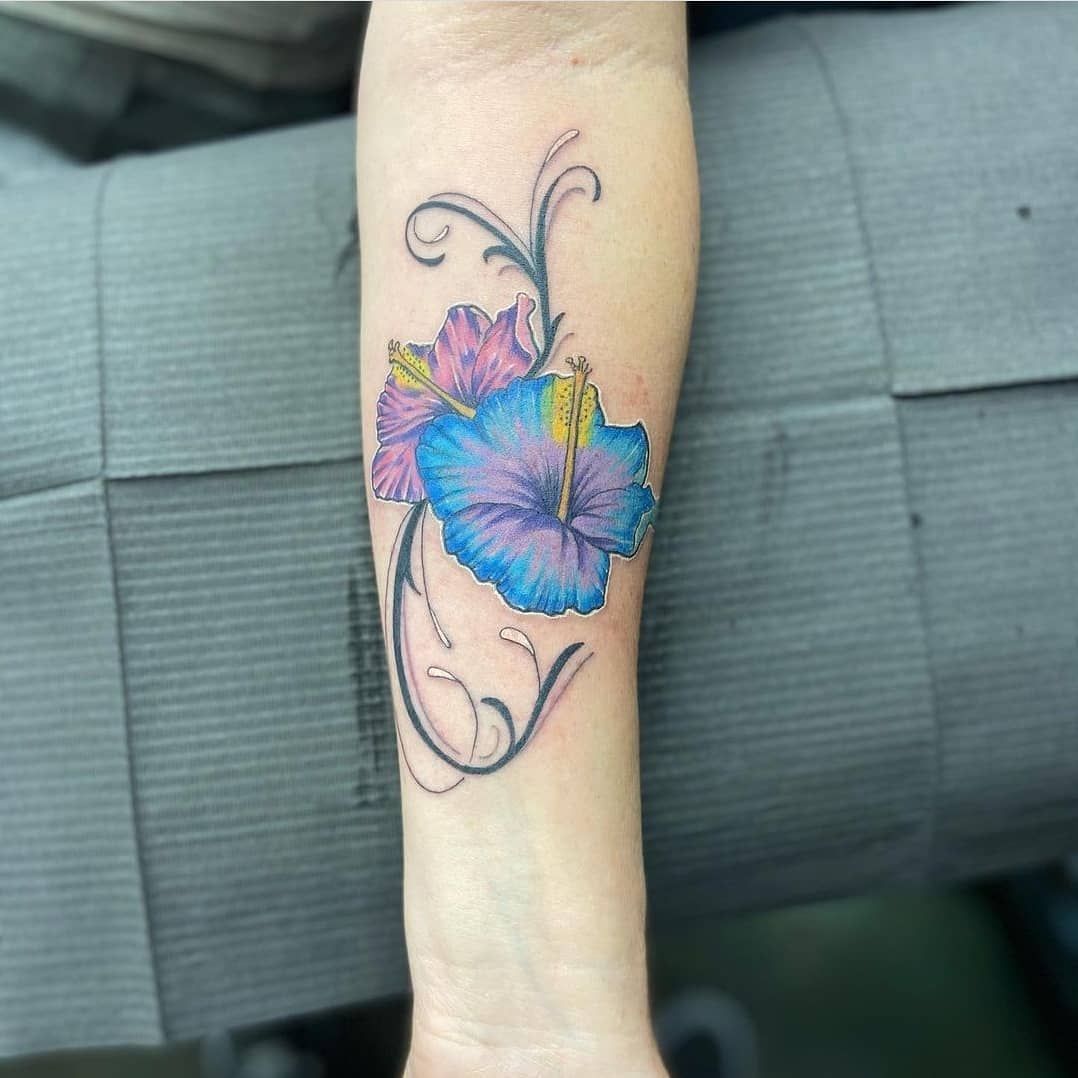 A woman has a blue and purple flower tattoo on her forearm