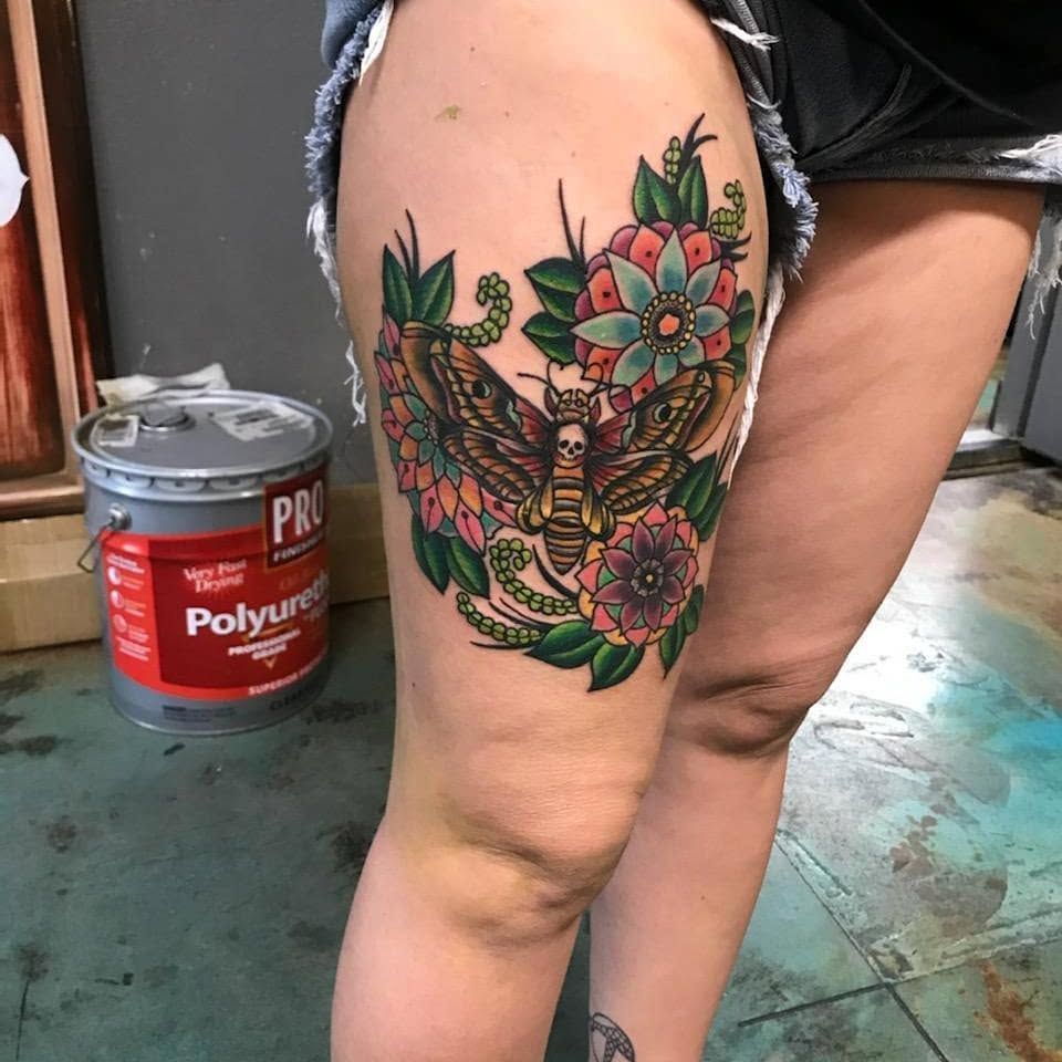A woman has a tattoo of a butterfly and flowers on her thigh