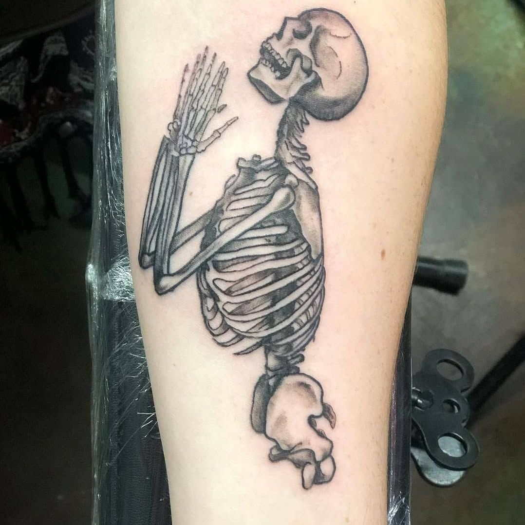A black and white tattoo of a skeleton on a person 's arm