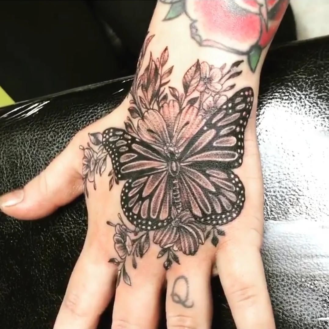 A woman has a tattoo of a butterfly and flowers on her hand