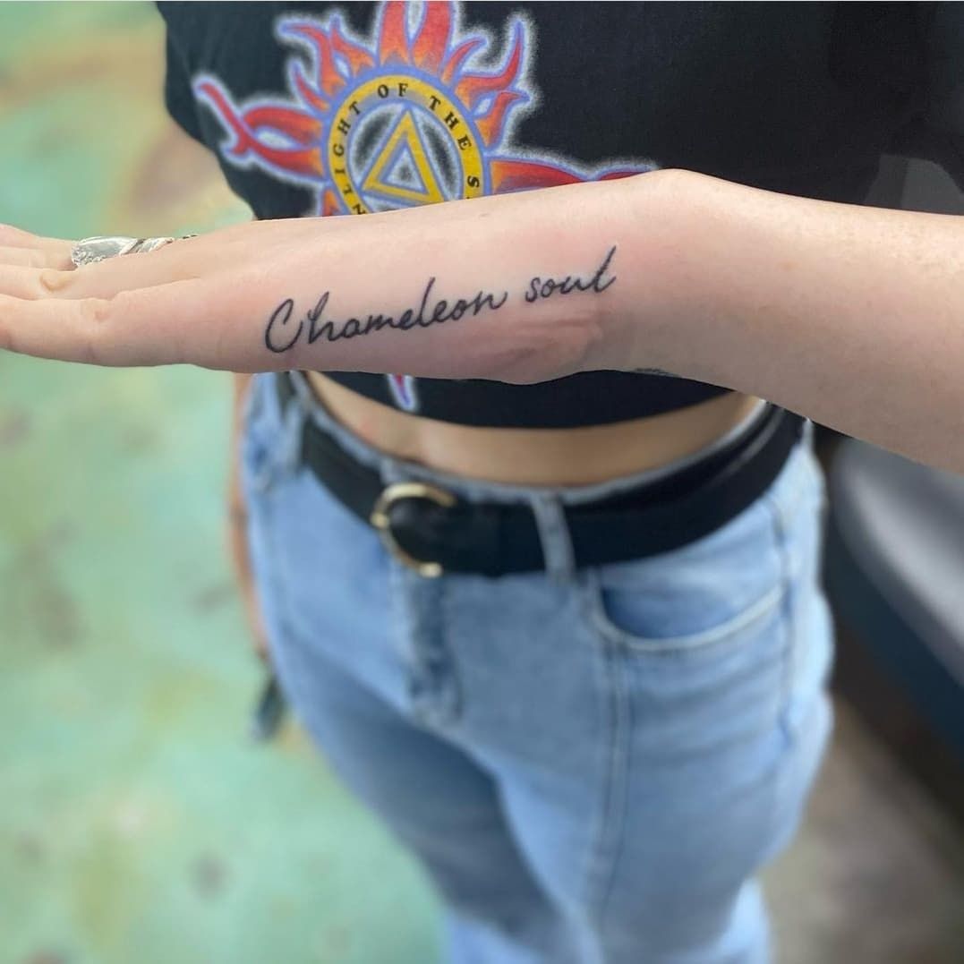 A woman has a tattoo on her arm that says chameleon soul