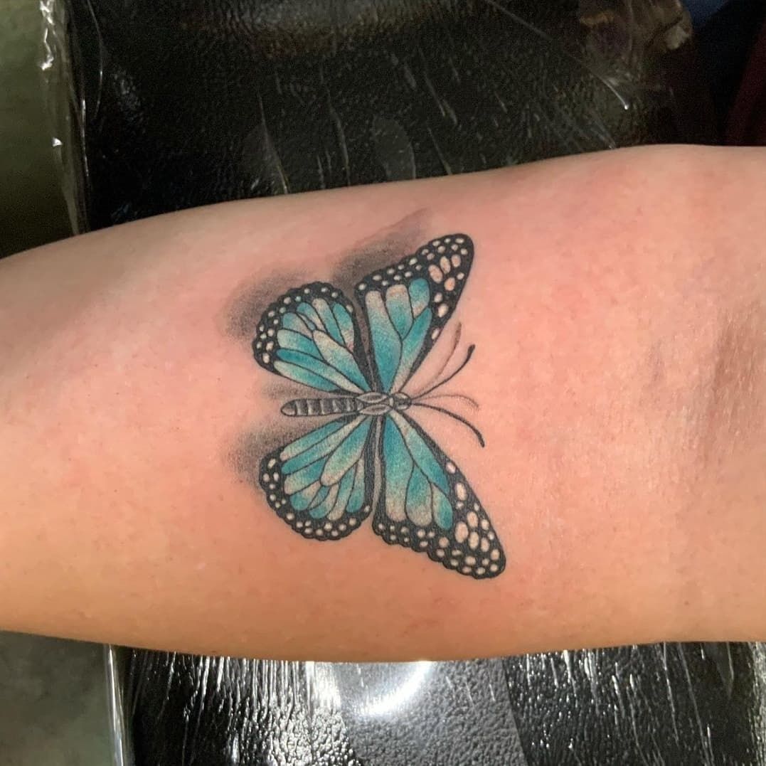 A person has a blue butterfly tattoo on their forearm.