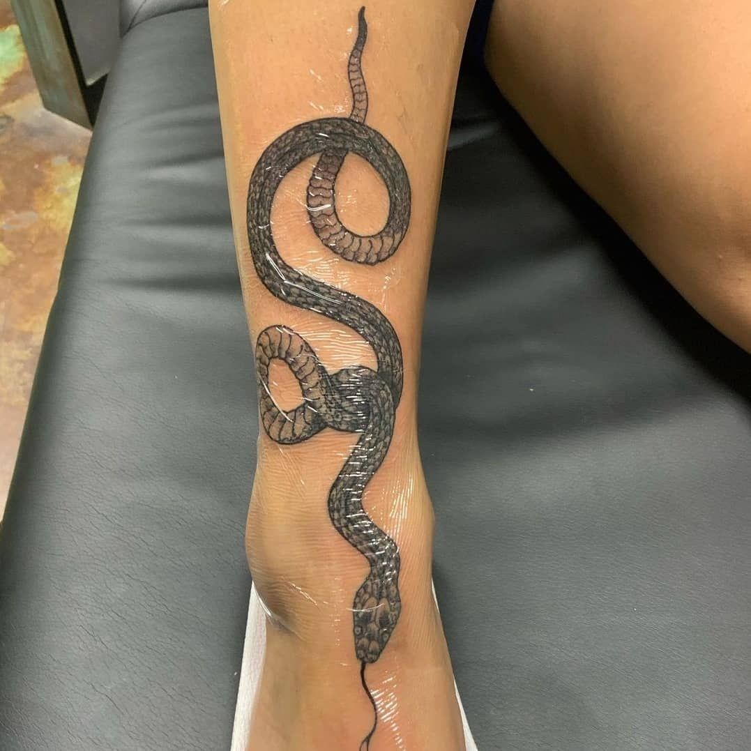 A woman has a tattoo of a snake on her leg