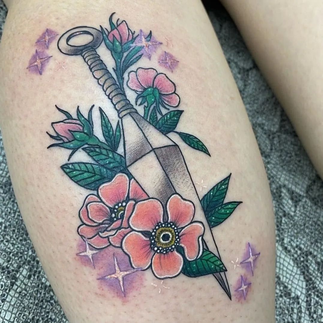 Tattoo of a dagger with pink flowers and green leaves on skin