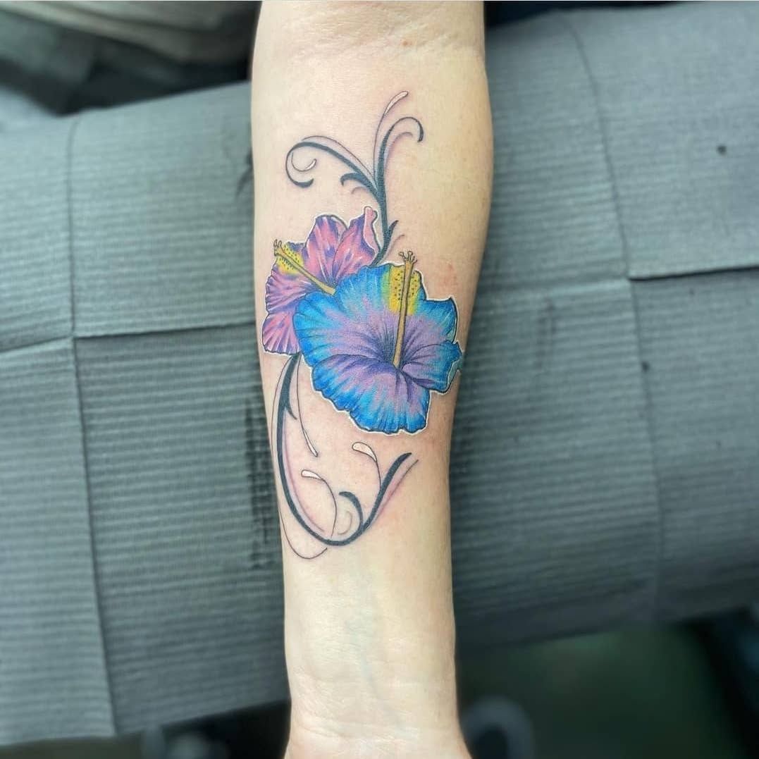 A woman has a blue and purple flower tattoo on her forearm