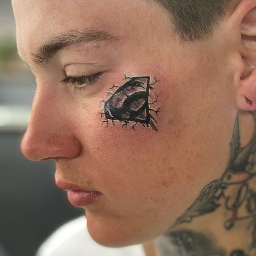 A man has a tattoo of the superman logo on his face.