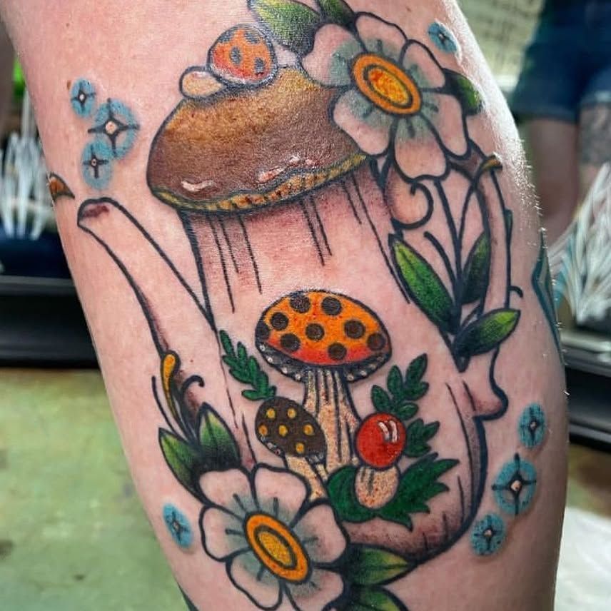 A tattoo of a teapot with mushrooms and flowers on it