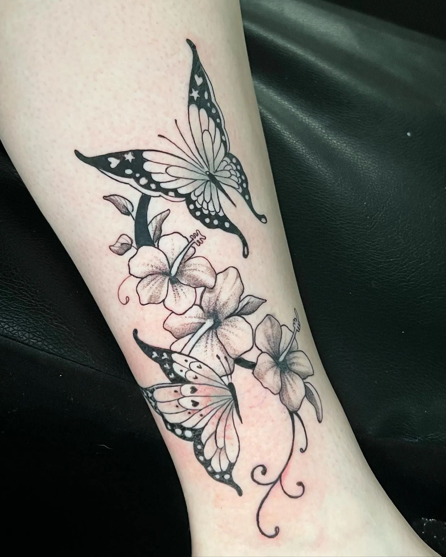 Butterfly and flower tattoo on an arm, black ink with details of petals and wings.