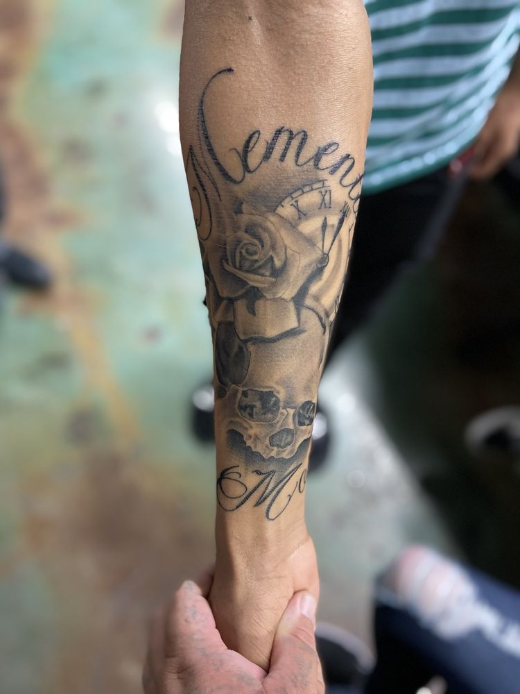 A person has a tattoo on their forearm with roses and the word cement.