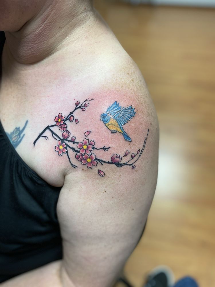A woman has a tattoo of a bird and flowers on her shoulder.