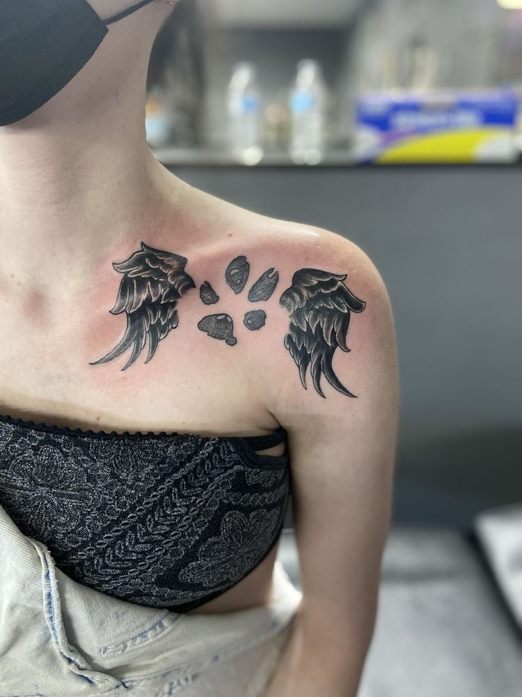A woman has a tattoo of wings and paw prints on her shoulder.