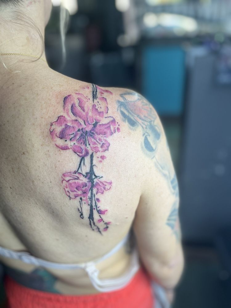 A woman has a tattoo of pink flowers on her back.