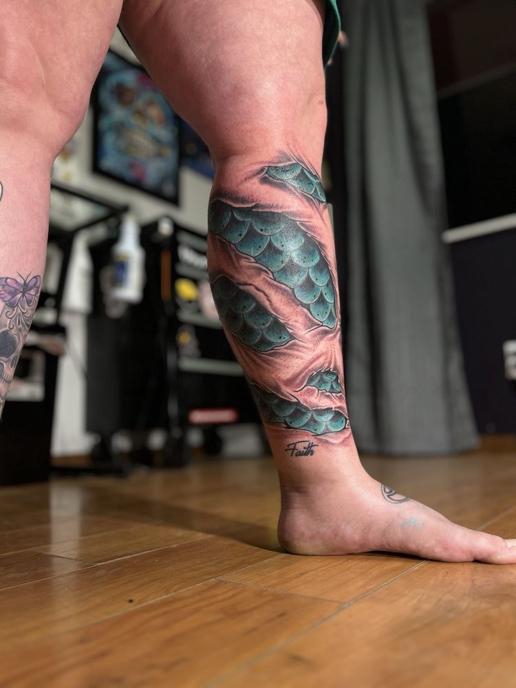 A woman with a tattoo on her leg is standing on a wooden floor.